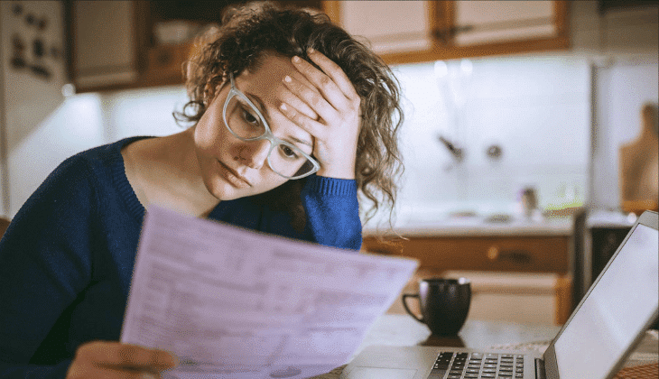 Worried woman reviewing bills at kitchen table with laptop open
